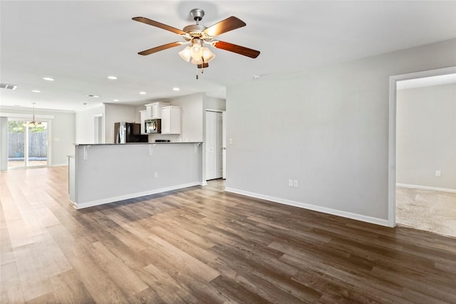 unfurnished living room featuring ceiling fan with notable chandelier and hardwood / wood-style flooring