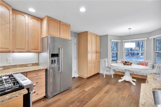 kitchen with decorative backsplash, appliances with stainless steel finishes, hanging light fixtures, and light brown cabinets