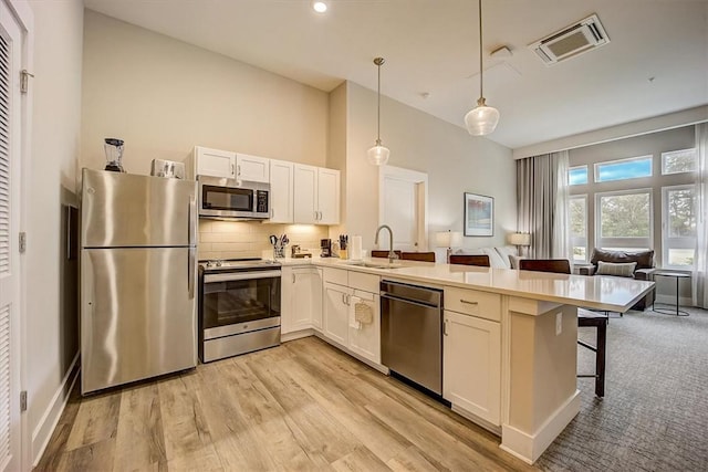 kitchen with stainless steel appliances, sink, white cabinetry, pendant lighting, and a breakfast bar