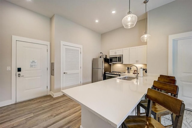 kitchen featuring stainless steel appliances, sink, white cabinets, a breakfast bar area, and pendant lighting