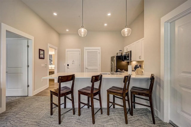 kitchen featuring stainless steel appliances, kitchen peninsula, a breakfast bar, white cabinets, and decorative light fixtures