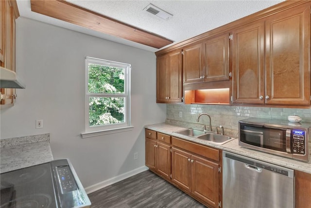 kitchen with stainless steel appliances, sink, backsplash, light stone countertops, and dark wood-type flooring