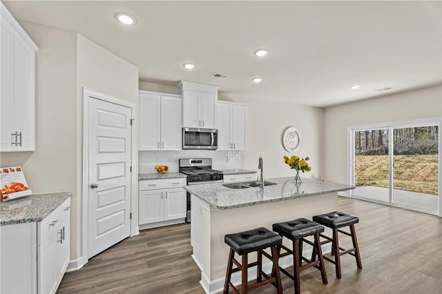 kitchen featuring stainless steel appliances, sink, white cabinets, wood-type flooring, and a center island with sink