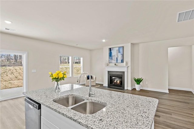 kitchen with light stone counters, stainless steel dishwasher, white cabinetry, and sink