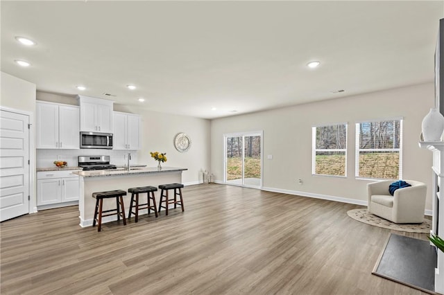 kitchen with a kitchen breakfast bar, a center island with sink, appliances with stainless steel finishes, light hardwood / wood-style floors, and white cabinets