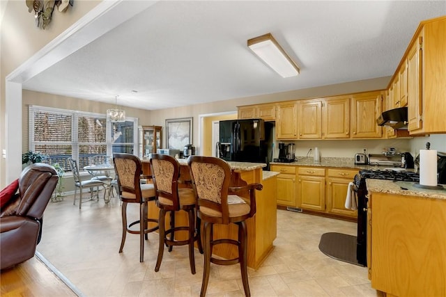 kitchen featuring black appliances, a center island, light stone countertops, a notable chandelier, and pendant lighting