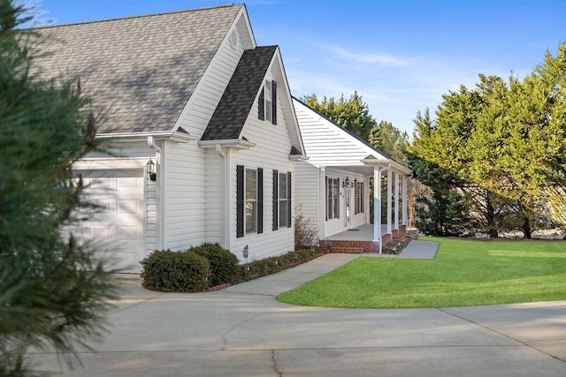 view of side of home featuring covered porch, a yard, roof with shingles, and a garage