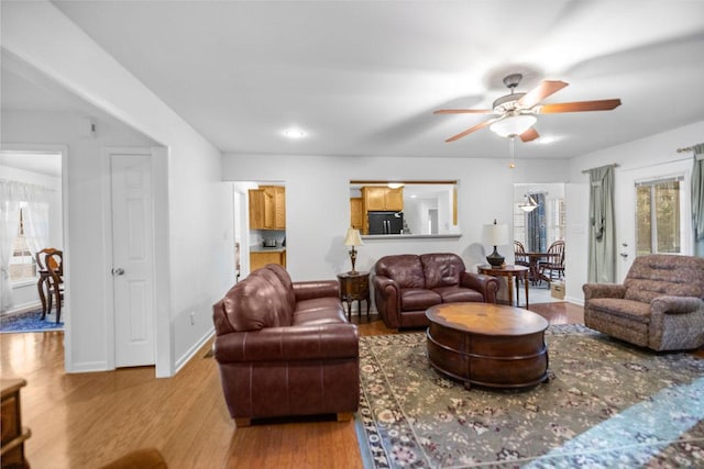 living area with light wood-style floors, ceiling fan, and baseboards