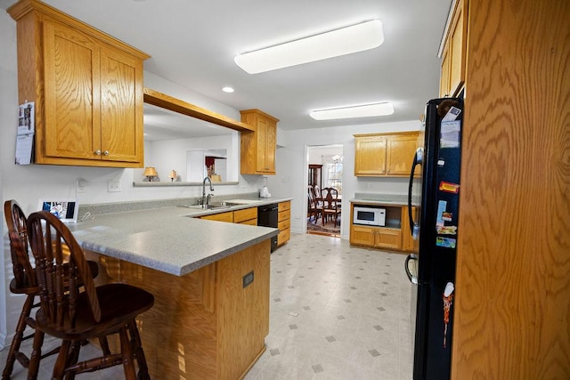 kitchen featuring white microwave, a breakfast bar area, freestanding refrigerator, a peninsula, and light floors