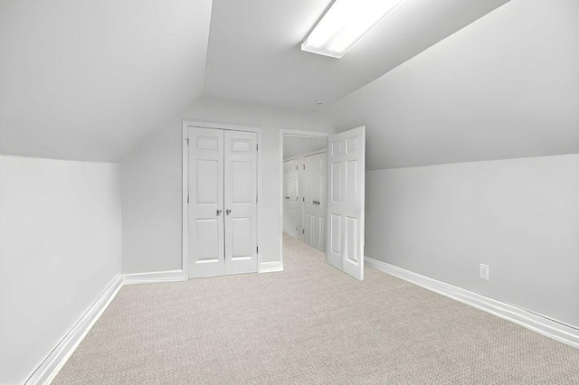 additional living space featuring baseboards, lofted ceiling, and light colored carpet