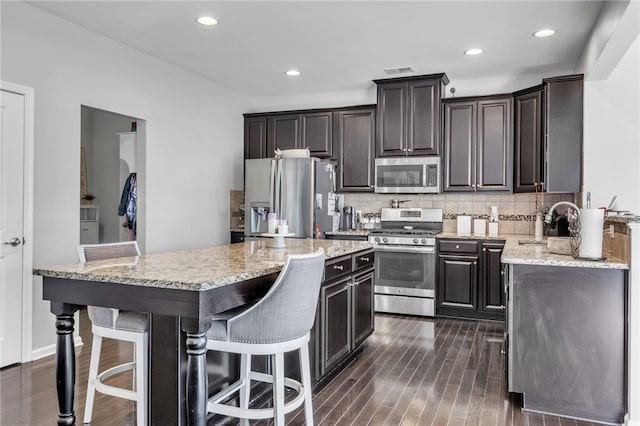 kitchen with stainless steel appliances, a center island, dark brown cabinetry, and a breakfast bar area