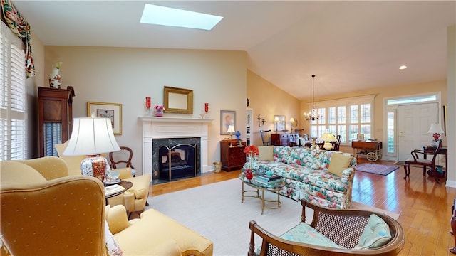 living room with a high end fireplace, lofted ceiling with skylight, a notable chandelier, and light hardwood / wood-style flooring