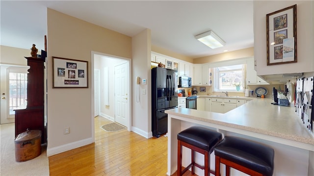 kitchen with white cabinetry, a kitchen bar, black appliances, light hardwood / wood-style flooring, and sink