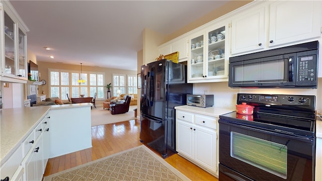 kitchen featuring light hardwood / wood-style floors, white cabinets, hanging light fixtures, and black appliances