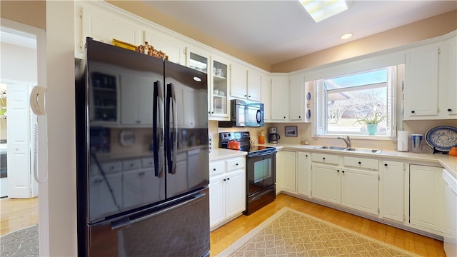 kitchen with sink, white cabinetry, black appliances, and light hardwood / wood-style flooring