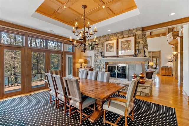 dining space featuring french doors, an inviting chandelier, a stone fireplace, light wood-type flooring, and a tray ceiling