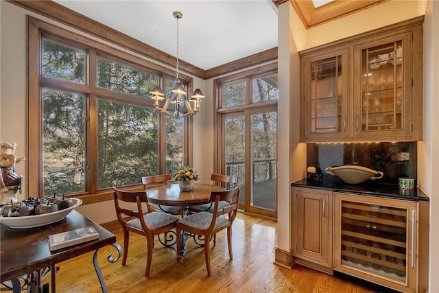 dining room featuring light wood-type flooring, beverage cooler, an inviting chandelier, and ornamental molding