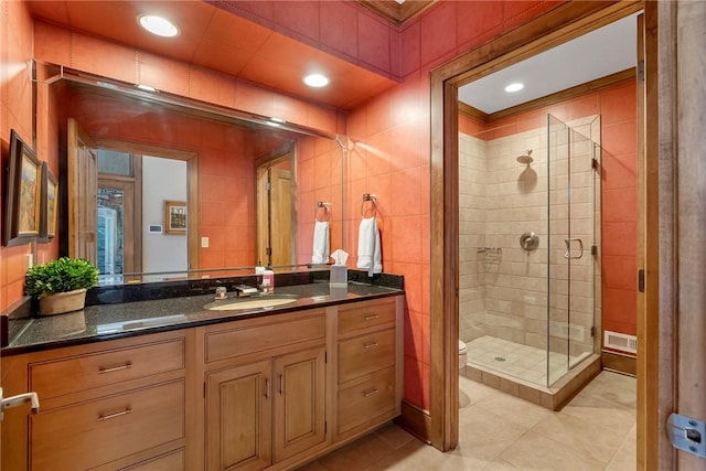 bathroom with toilet, a shower with door, tile patterned flooring, tile walls, and vanity