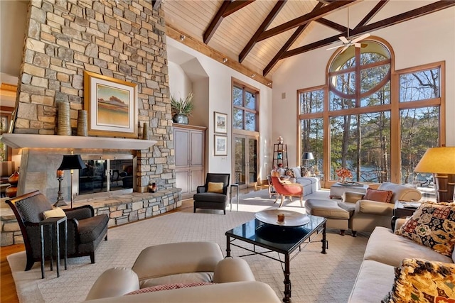 living room with beamed ceiling, a fireplace, ceiling fan, light wood-type flooring, and high vaulted ceiling