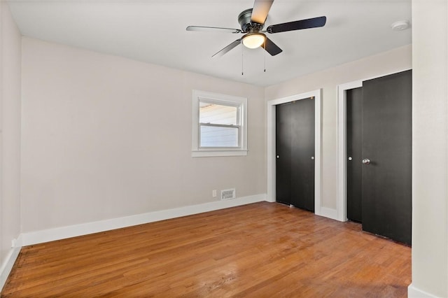 unfurnished bedroom with ceiling fan, light hardwood / wood-style floors, and multiple closets