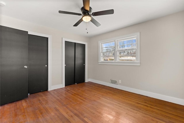 unfurnished bedroom with ceiling fan, hardwood / wood-style floors, and multiple closets