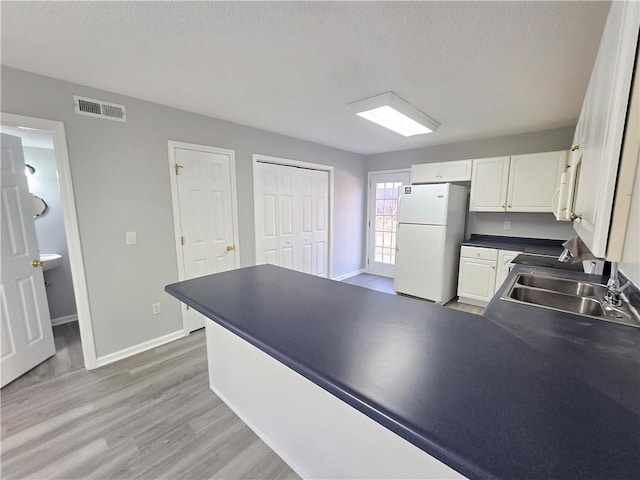 kitchen with a textured ceiling, white cabinetry, white refrigerator, wood-type flooring, and sink