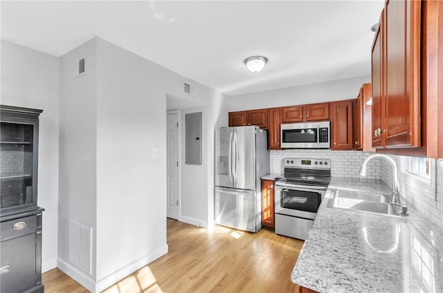 kitchen with appliances with stainless steel finishes, light wood-type flooring, light stone counters, sink, and backsplash