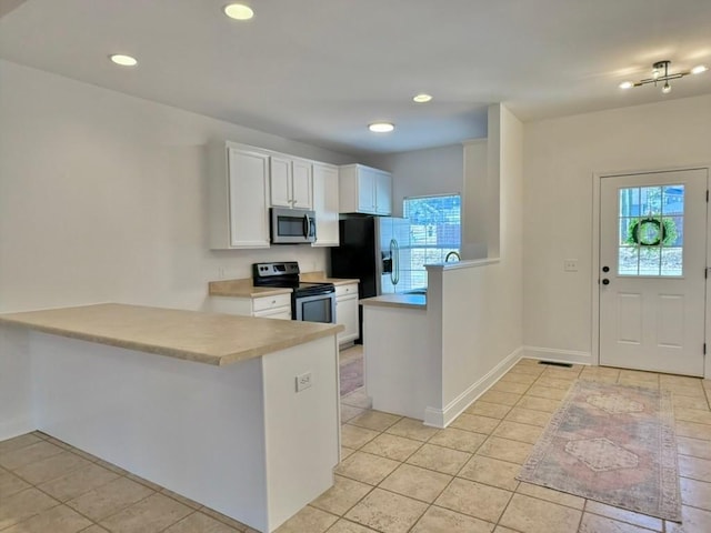 kitchen featuring kitchen peninsula, appliances with stainless steel finishes, light tile patterned floors, and white cabinetry