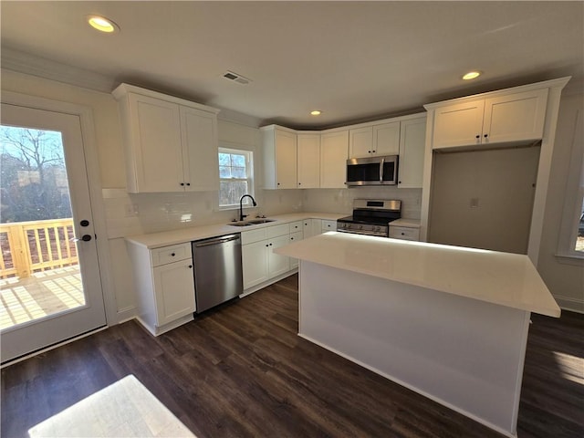 kitchen with a center island, backsplash, white cabinets, appliances with stainless steel finishes, and sink