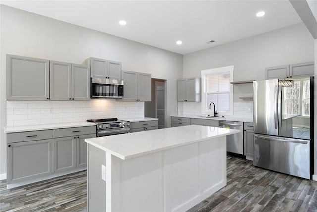 kitchen with stainless steel appliances, gray cabinets, light countertops, a kitchen island, and a sink