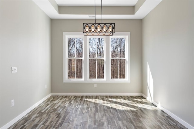 unfurnished dining area with a tray ceiling, baseboards, and wood finished floors