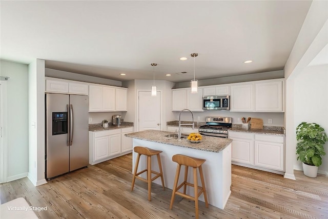 kitchen featuring an island with sink, appliances with stainless steel finishes, pendant lighting, white cabinets, and sink