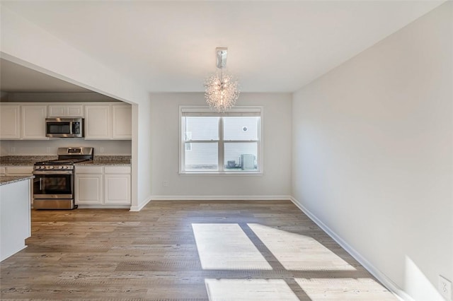 kitchen featuring decorative light fixtures, an inviting chandelier, light wood-type flooring, appliances with stainless steel finishes, and white cabinets