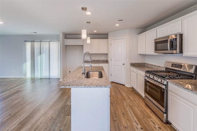 kitchen with pendant lighting, appliances with stainless steel finishes, white cabinets, an island with sink, and sink