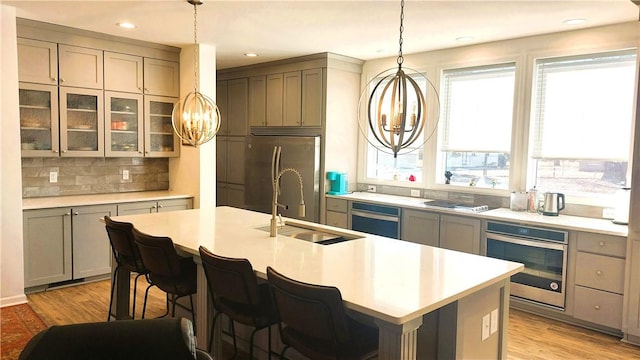 kitchen featuring a kitchen island with sink, light wood-type flooring, stainless steel appliances, and an inviting chandelier