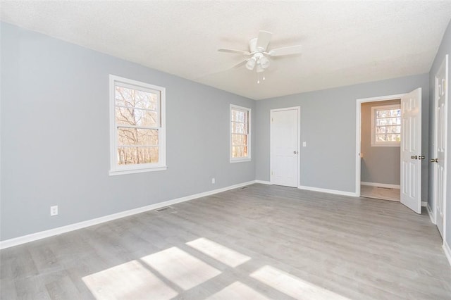 unfurnished bedroom with ceiling fan, a textured ceiling, multiple windows, and light hardwood / wood-style flooring