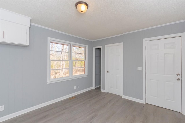 unfurnished bedroom featuring light hardwood / wood-style floors, a textured ceiling, and crown molding