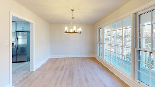 unfurnished dining area with a notable chandelier and light wood-type flooring