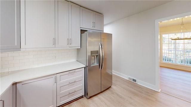 kitchen with backsplash, stainless steel fridge with ice dispenser, a chandelier, and light hardwood / wood-style floors