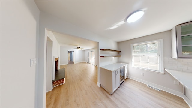 kitchen featuring white cabinetry, ceiling fan, beverage cooler, a fireplace, and light hardwood / wood-style flooring