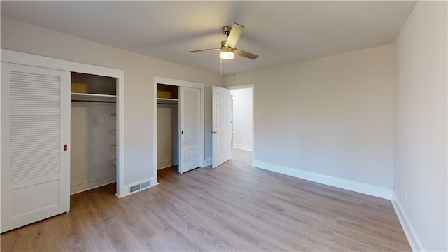 unfurnished bedroom featuring ceiling fan, light hardwood / wood-style floors, and multiple closets