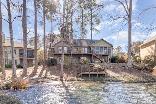 rear view of property with a deck with water view and a sunroom