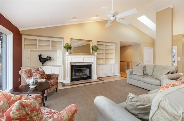 living room featuring ceiling fan, vaulted ceiling with skylight, built in features, and crown molding