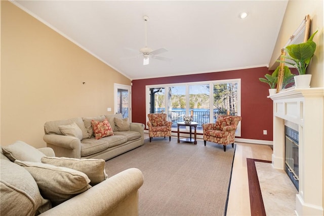 living room featuring a high end fireplace, light hardwood / wood-style floors, vaulted ceiling, ceiling fan, and crown molding