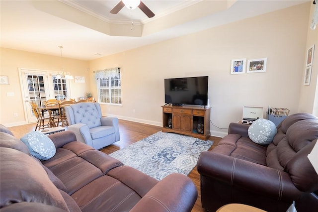 living room featuring ornamental molding, ceiling fan with notable chandelier, a tray ceiling, wood finished floors, and baseboards