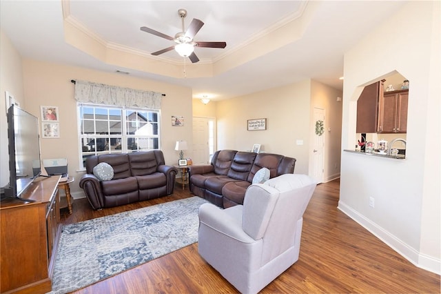 living room with a tray ceiling, baseboards, wood finished floors, and crown molding