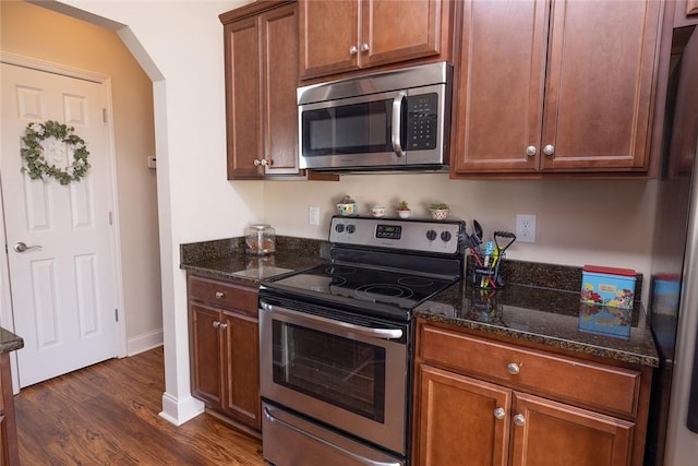 kitchen with dark stone countertops, arched walkways, dark wood-style flooring, and stainless steel appliances