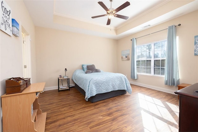 bedroom with a raised ceiling, wood finished floors, baseboards, and ornamental molding