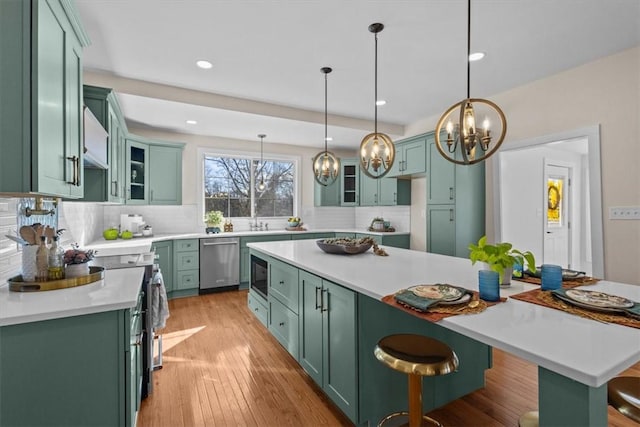 kitchen with decorative light fixtures, backsplash, a kitchen island, a kitchen bar, and appliances with stainless steel finishes