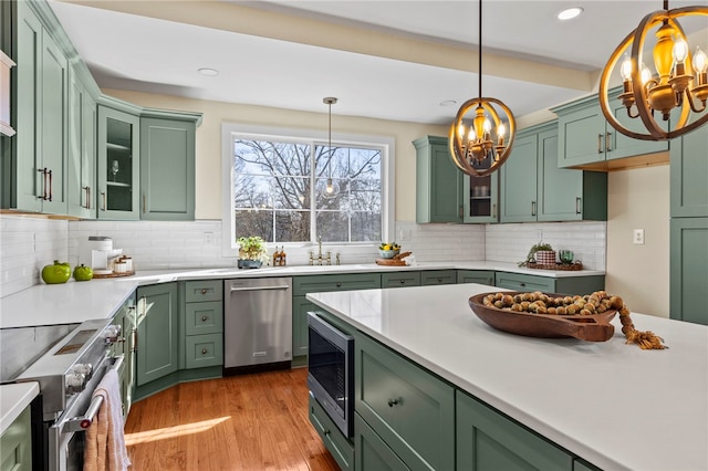 kitchen featuring glass insert cabinets, light countertops, hanging light fixtures, and appliances with stainless steel finishes